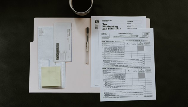 A table holds a folder and tax forms. A pen and cup of coffee are positioned nearby.